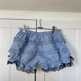 Blue ruffled shorts with black lace trim hanging on a rack against a white wooden panel background.
